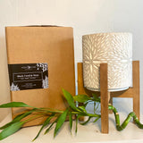 This image is  a natual color  Corrugated shopping box for  10 1/2 " tall   Black Coral and moss  Candle  in grey concrete with a  brown wooden pedestal  on floral background. Our Black Coral and Moss scent  is  Sensual and masculine, It  marries notes of lavender, amber, dark musk, and vetiver. The wax is  Coconut Apricot Creme with  48 OZ  of  Black Coral and Moss scented wax Available from  Wild Orchid Candle Company